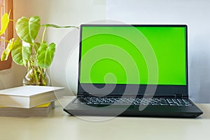 Laptop computer showing chroma green screen on LCD display stands on a desk with books next to ready for further design and copy