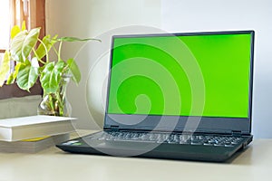 Laptop computer showing chroma green screen on LCD display stands on a desk with books next to ready for further design and copy