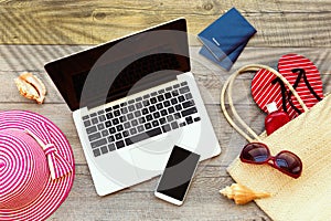 Laptop computer and smart phone with beach accessories on wooden board