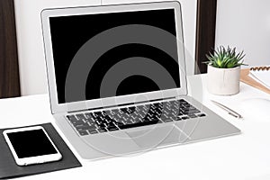 Laptop computer and smartphone with blank mock up screens are on top of white office desk table