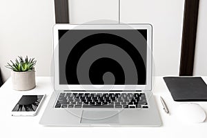 Laptop computer and smartphone with blank mock up screens are on top of white office desk table