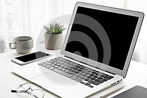 Laptop computer and smartphone with blank mock up screens are on top of white office desk table