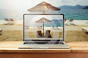 Laptop computer with sunny beach image on wooden table. Summer vacation photo