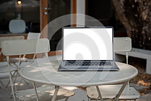 A laptop computer with a white-screen mockup is on an outdoor table of a coffee shop