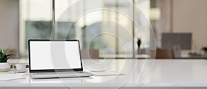 A laptop computer with a white-screen mockup on a table in a modern office