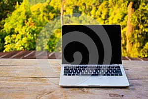 Laptop computer on wooden table terrace with beautiful outdoor background nature landscape scenery forest and mountain valley in