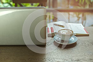 Laptop and cup of coffee and cell phone with books and pen on wooden table