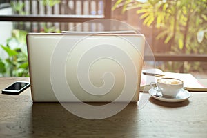 Laptop and cup of coffee and cell phone with books and pen on wooden table