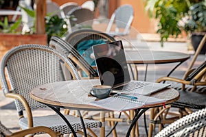 Laptop, a cup of coffee and a notebook with a pen on a table in an outdoor cafe