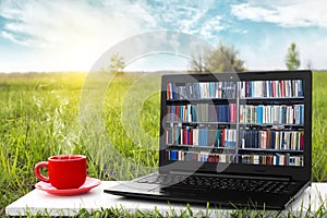 Laptop and cup of hot coffee on the background picturesque nature, outdoor office. E-book library concept. Internet books store.