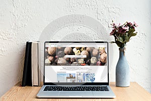 laptop with depositphotos website on screen books and flowers in vase