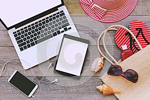 Laptop, digital tablet and smart phone with beach items over wooden background. View from above