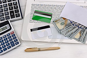 Laptop with dollars in envelope and credit cards