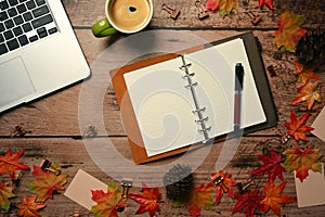 Laptop, empty notebook, coffee cup and autumn maple leaves on wooden table.