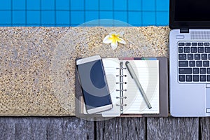 Laptop and empty notebook on the edge of swimming pool