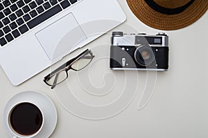 Laptop, eyeglasses, camera, hat and a cup of coffee on white sur