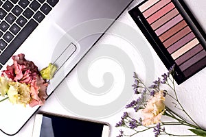 Laptop with flowers and cosmetics on white table. Freelancer workspace