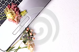 Laptop with flowers and cosmetics on white table. Freelancer workspace