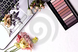 Laptop with flowers and cosmetics on white table. Freelancer workspace