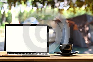 Laptop on folding picnic table near camp tent outdoors.