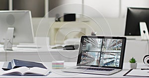 Laptop with four security camera views on screen on desk in empty modern office space, slow motion