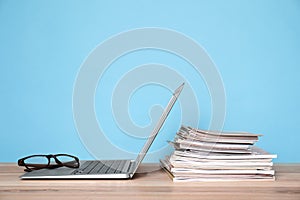 Laptop, glasses and stack of magazines on wooden table