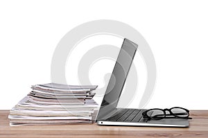 Laptop, glasses and stack of magazines on wooden table
