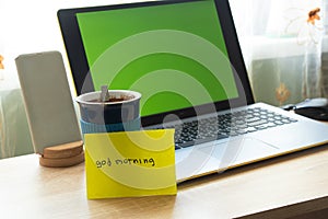 Laptop with green screen cup with coffee table and the inscription good morning in the room