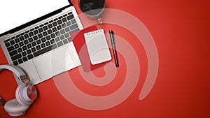 Laptop, headphone, notebook and coffee cup on red background.