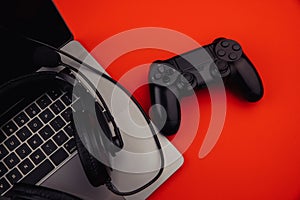Laptop with headphones, black gamepad on red background. Gaming and cybersport concept