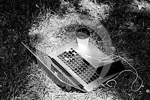 Laptop with headset of mobile phone and coffee to go on green grass. agile business. Online study. summer vibes. Relax