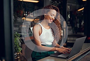 Laptop, internet cafe and typing with a black woman blogger working at the window of a coffee shop on an article or