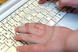 a laptop keyboard with English and Arabic Alphabet with an out of focus child's hand typing on a white keyboard