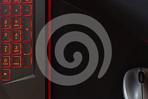 Laptop keyboard with red backlight, computer mouse on a black mouse pad