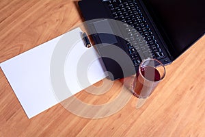 Laptop keyboard, white paper and a glass of juice on a wooden table. Blank space for your copy text