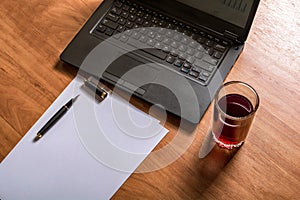 Laptop keyboard, white paper, ink pen and a glass of juice on a wooden table. Blank space for your copy text