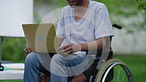 Laptop on knees of disabled man in wheelchair with unrecognizable blurred African American crippled invalid talking at