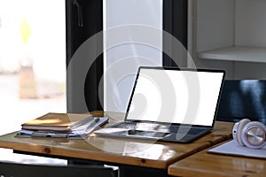 Laptop with lank screen, notebook, headphone and documents on wooden desk.