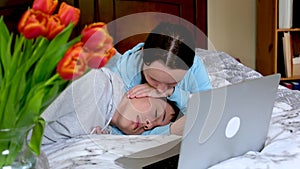 laptop lie on bed tulips silhouette two toung lovers touching, ambracing and kissing each other soft and tenderly