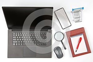 Laptop, magnifying glass, computer mouse, smartphone, pen, notepad and grocery basket on a white background. Items for business