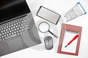 Laptop, magnifying glass, computer mouse, smartphone, pen, notepad and grocery basket on a white background. Items for business