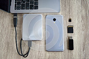 Laptop and mobile phone data transfer peripherals - portable HDD, usb flash drive and SD cards - lying on a wooden table photo