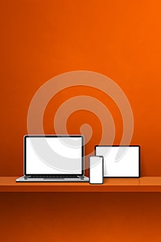 Laptop, mobile phone and digital tablet pc on orange wall shelf. Vertical background