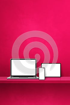 Laptop, mobile phone and digital tablet pc on pink wall shelf. Vertical background