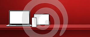 Laptop, mobile phone and digital tablet pc on red wall shelf. Banner background