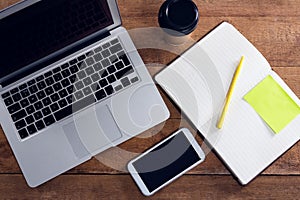 Laptop, mobile phone, disposable glass, pen and organizer on wooden table