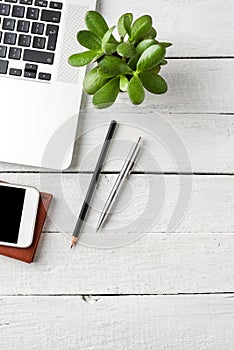 Laptop, mobile phone, notebook, pen and small flower on white wooden desktop.