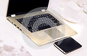 Laptop with Mobile Phone and tea cup on table. Closeup view.