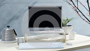 Laptop Mock-Up on work desk beside wall with plant beside it. Side light shadows the trees.