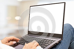 Laptop mockup with blank white screen, woman holds laptop on her knees lying on sofa at home. woman sits on her lap with laptop in